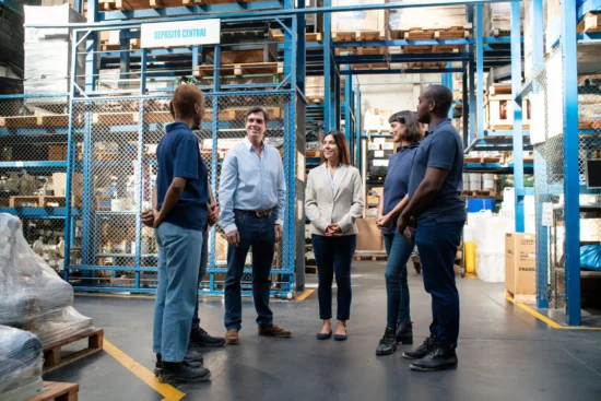 Professional team meeting in a central food distribution depot with blue storage racks and inventory boxes, showcasing wholesale food supply management.
