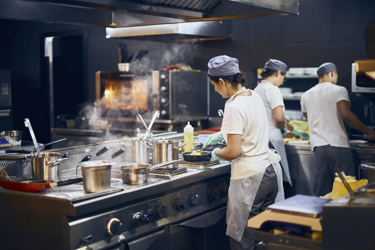 Chefs preparing food on a commercial stainless steel range in a professional kitchen, ideal for foodservice supply.