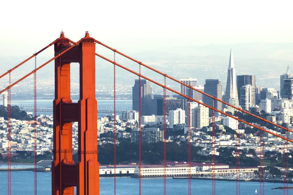 Golden Gate Bridge frames San Francisco's downtown skyline with bay waters below, iconic architectural landmark.